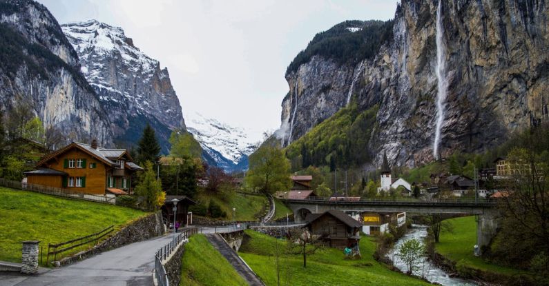 Waterfall Way - Asphalt walkway near wild river in scenic countryside with small chalets amidst powerful snowy rocky mountains in Lauterbrunnen valley